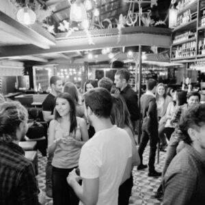 Crowd of people standing around a bar drinking alcohol and socializing