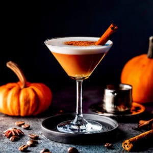 simple fall cocktail of pumpkin spice espresso martini sitting ona table surrounded by pumpkins and fall spices